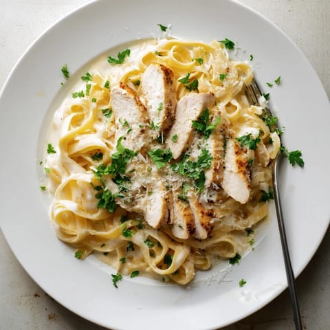 Steaming plate of homemade fettuccine Alfredo served with golden, sliced sautéed chicken breast for a hearty dinner.