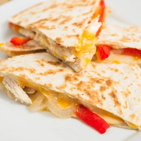 A freshly cooked Chicken Quesadilla sliced into triangles, revealing layers of grilled chicken and gooey cheese filling.