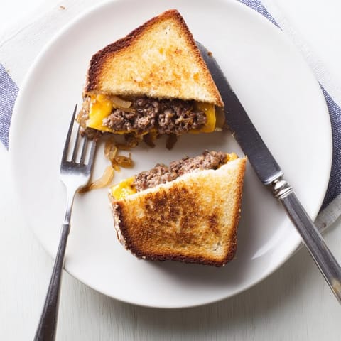 Close-up of a hot Patty Melt with melted cheese oozing from buttery grilled sourdough and savory beef patties.