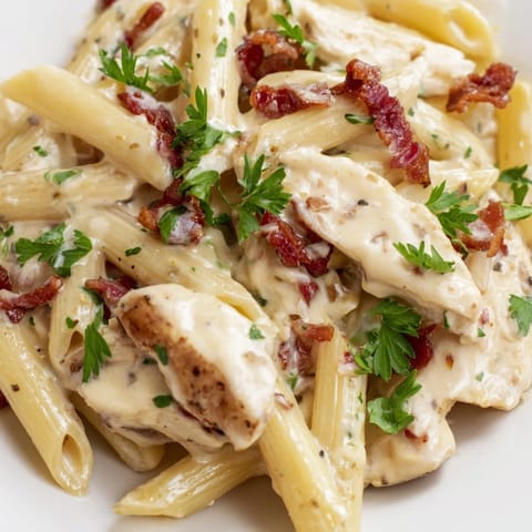 Creamy Chicken Bacon Penne served hot, garnished with fresh parsley and extra Parmesan, on a white plate with a side salad.