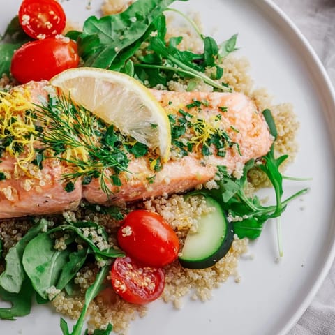 Freshly baked salmon fillets rest atop fluffy quinoa salad with tomatoes, cucumber, and zesty lemon herb dressing.