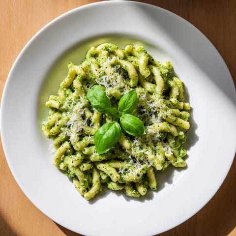 Freshly cooked macaroni is tossed in a vibrant green avocado pesto sauce, garnished with basil and grated Parmesan.  