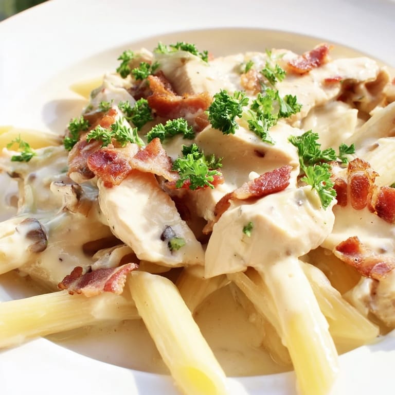 Creamy Chicken Bacon Penne twirled onto a fork, showcasing tender chicken, crispy bacon, and rich garlic-Parmesan cream sauce against a dark background.