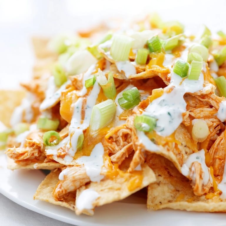 This Buffalo Chicken Nachos platter features bubbling cheese, green onions, and celery, served hot from the oven.  