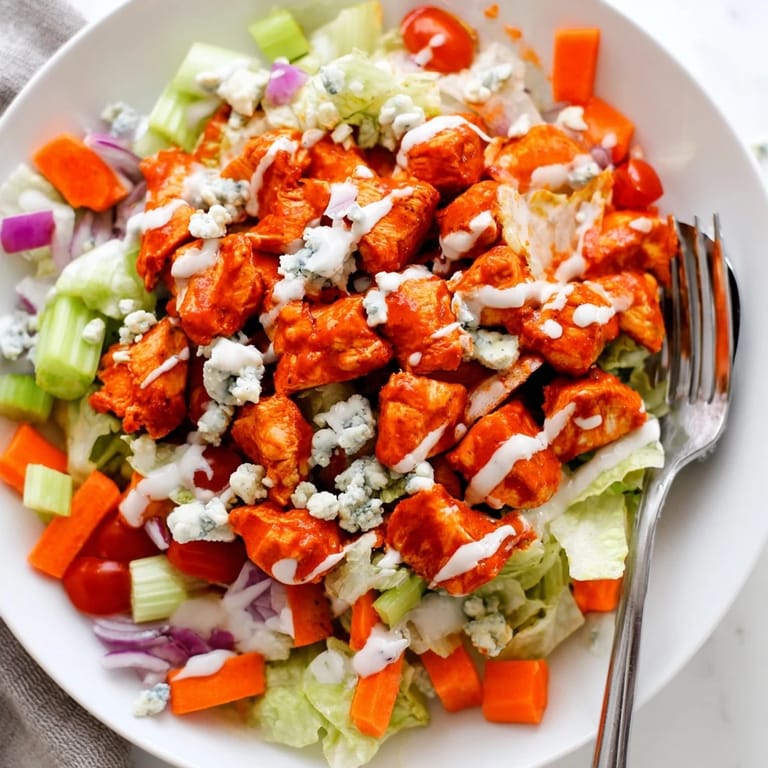 Spicy buffalo chicken pieces on a bed of chopped greens with blue cheese crumbles and a drizzle of ranch dressing.