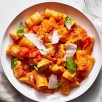 A close-up of Tomato Basil Chicken Pasta showing tender golden chicken pieces and al dente penne coated in a vibrant red tomato sauce with fresh basil.