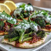 Roasted harissa broccoli florets with charred edges piled onto warm flatbreads, topped with creamy Greek yogurt and fresh cilantro.