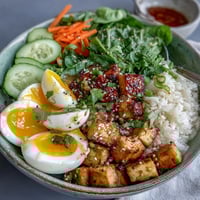 Tofu Jammy Egg Breakfast Bowl topped with halved soft eggs, crisp cucumbers, and toasted sesame seeds over warm rice.